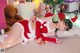 A woman in a santa outfit laying on the floor next to a teddy bear.