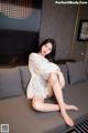 A woman sitting on a couch in a white dress.