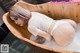 A woman in a white bodysuit is taking a bath in a wooden tub.